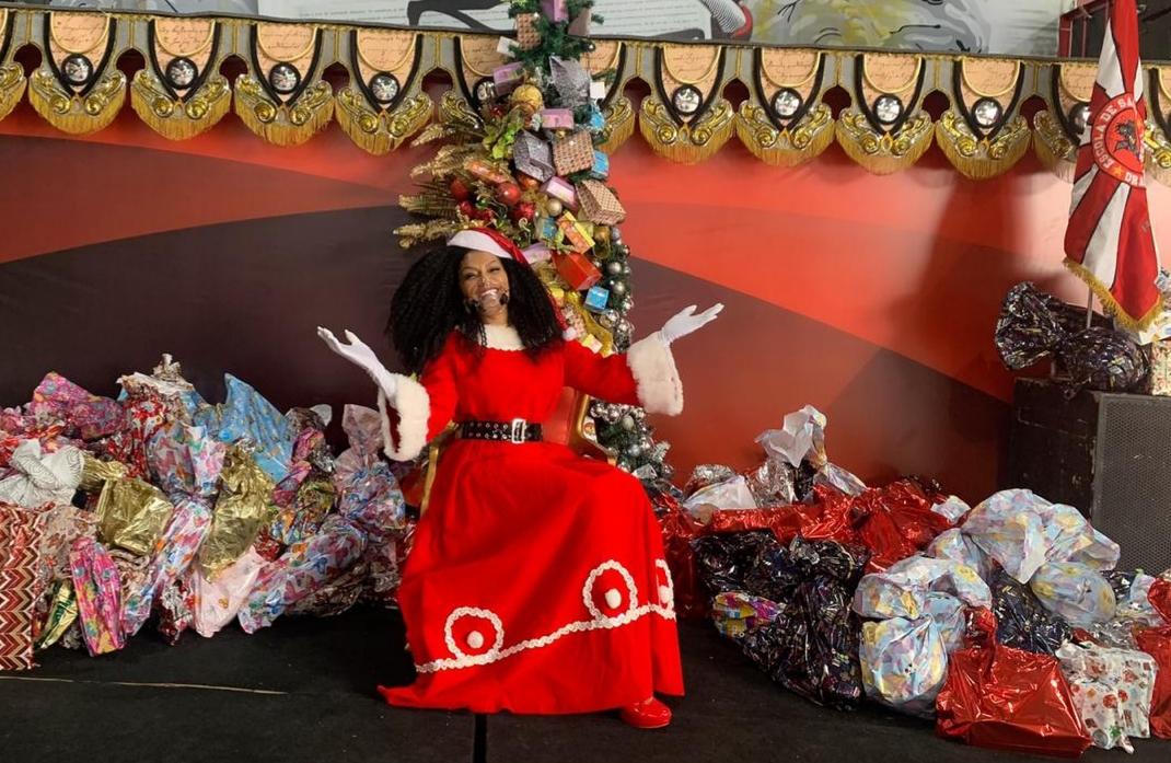 Simone Sampaio distribui presentes ao lado de Papai Noel de máscara na Dragões da Real